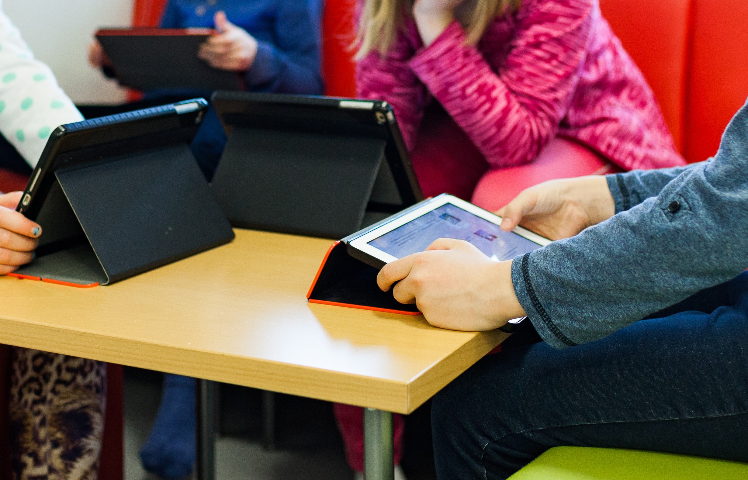Kuvassa lapsia istumassa pöydän ääressä tablet-tietokoneet käsissään.