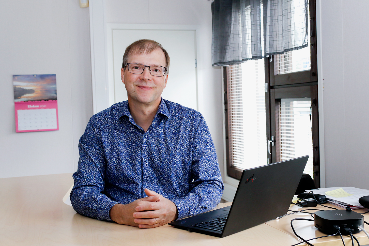 Kunnanjohtaja Heikki Hallikainen nojaa työpöytää vasten, hänen edessään on kannettava tietokone.